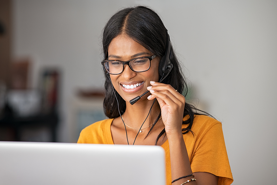 Cheerful indian woman in smart working from home. Happy middle eastern girl working as customer service representative with laptop. Smiling young woman with headset doing video call at home.